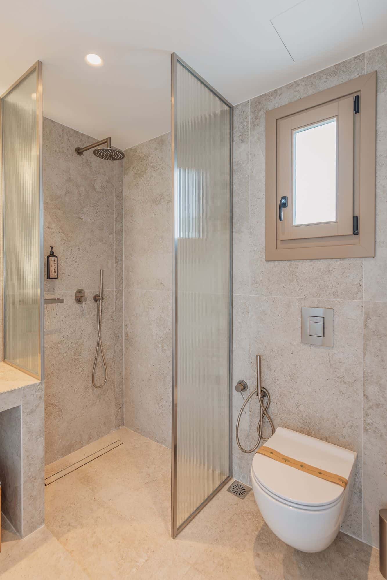 Bright, stylish Mykonos hotel bathroom featuring shower, toilet, and natural light.