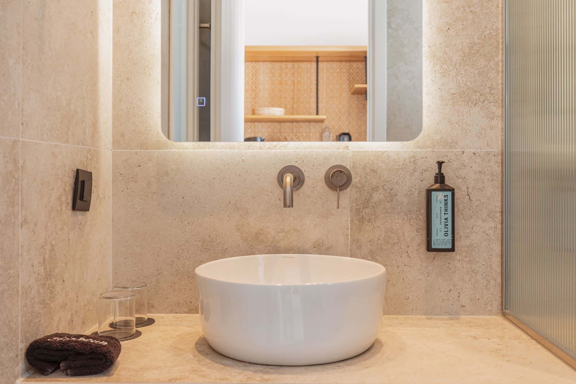Elegant bathroom vanity with a round white sink, wall-mounted faucet, and skincare product in Mykonos.
