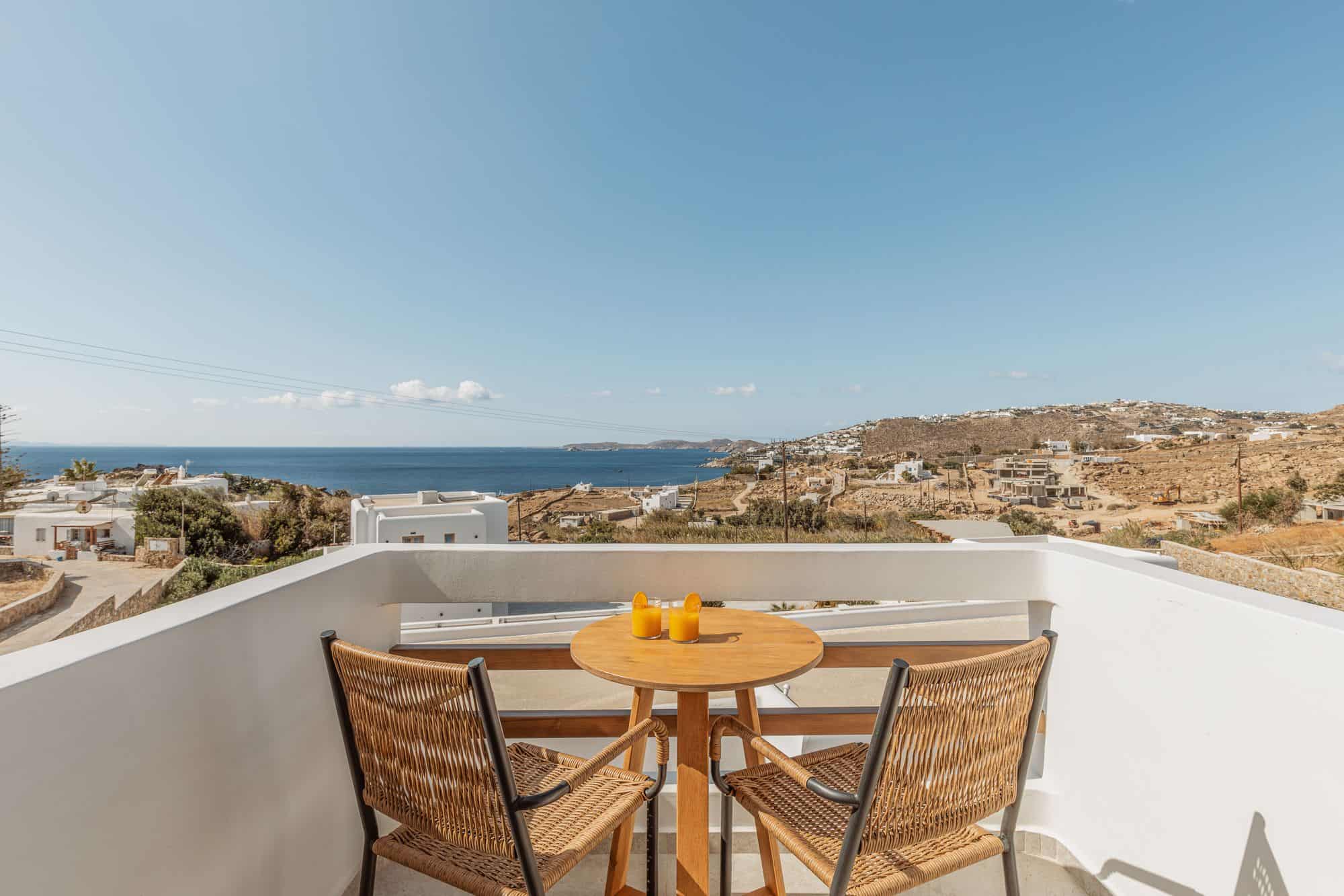 Stunning Mykonos balcony with ocean view, outdoor table, and vibrant sunshine, perfect for relaxing.
