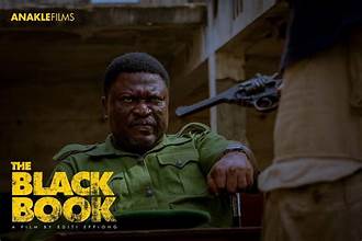 African movie star sitting outdoors with a gun in hand, intense expression, promotional image for the film The Black Book.