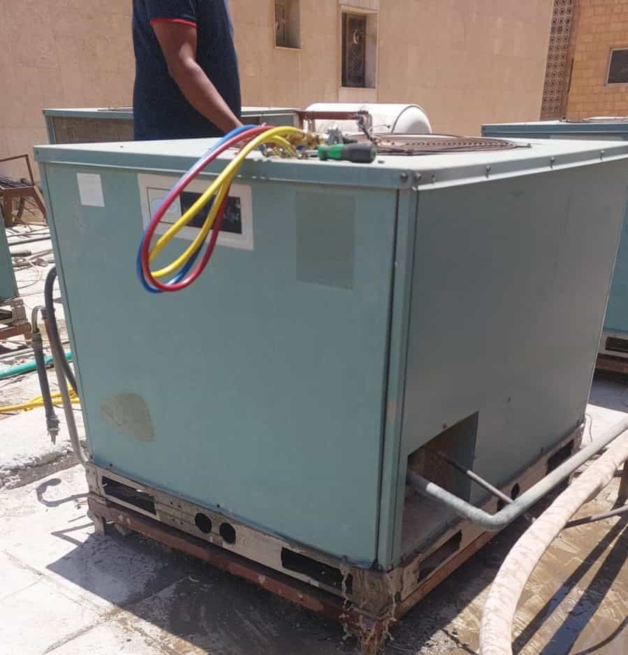 فني تكييف هندي بالكويت يقوم بصيانة وحدة تكييف مركزية على سطح المبنى.