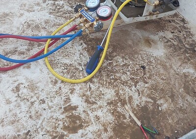 فني تكييف هندي بالكويت يقوم بصيانة وحدة تكييف مع أدوات ومعدات إصلاح على سطح المبنى.