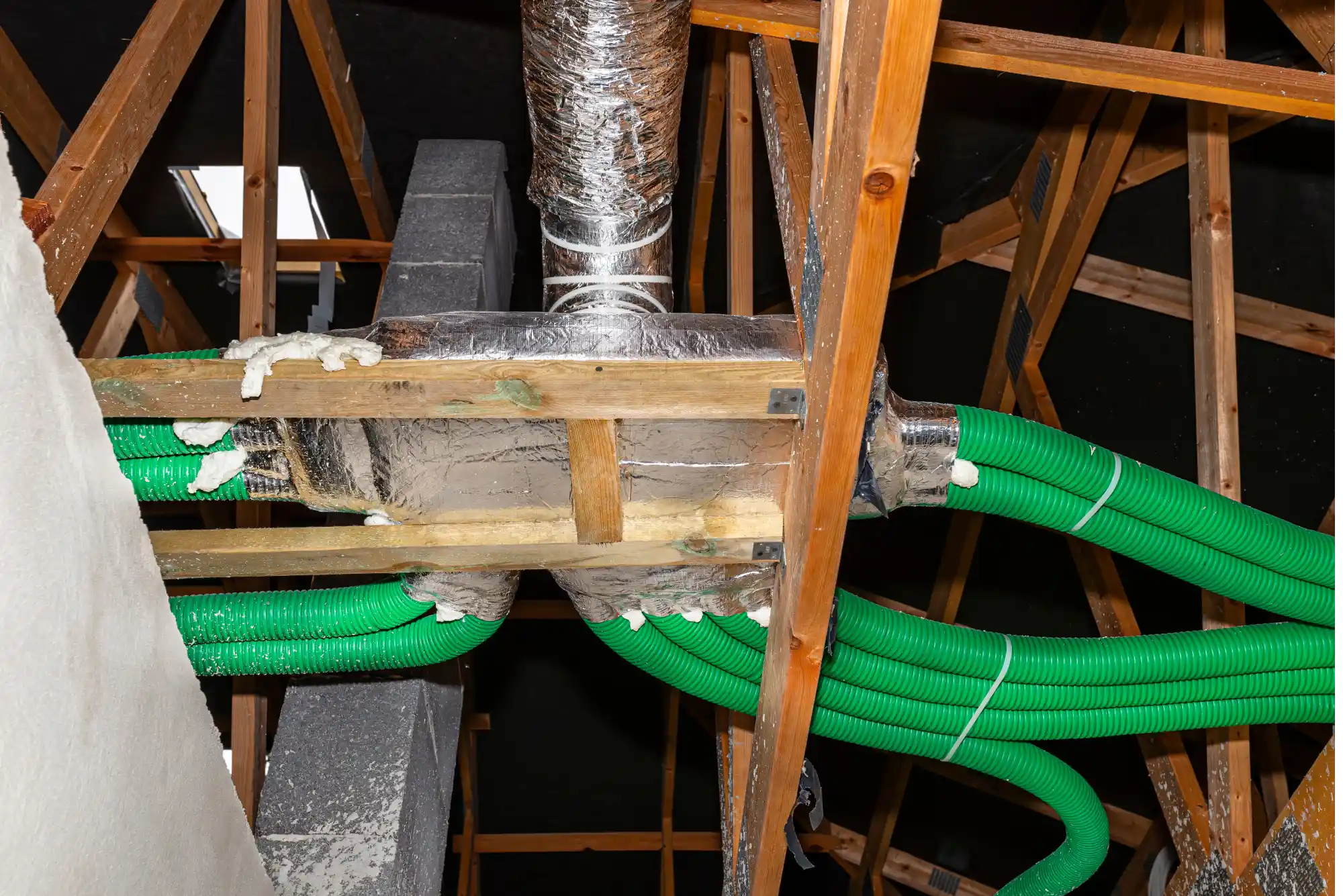 Green ventilation pipes and silver ductwork in a wooden attic frame