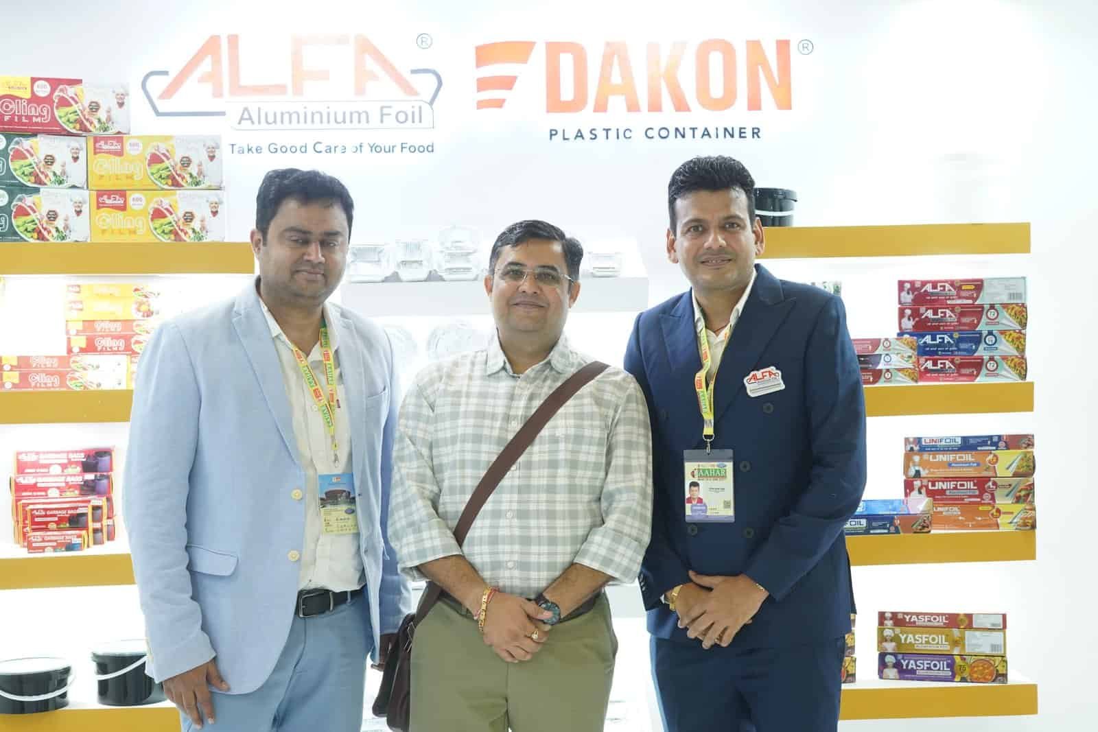 Three men standing in front of Alfa Foil Containers display at food packaging trade show.