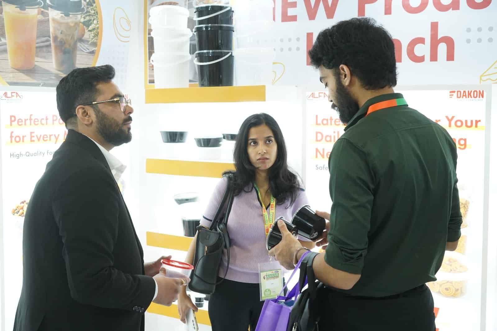 Three people discussing Alfa foil containers at a trade exhibition booth.