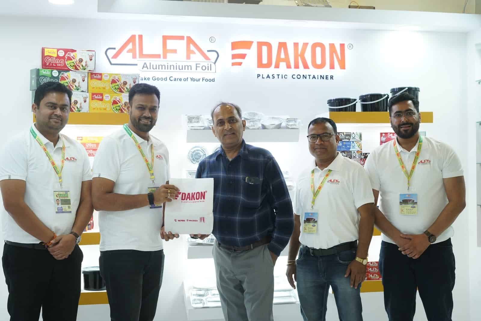 Group of men showcasing Alfa Foil Containers at trade show booth.