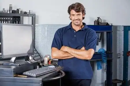 Technician smiling in a computer repair shop with tools and equipment.