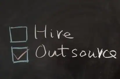 Outsource checkbox marked on a blackboard for IT support services.