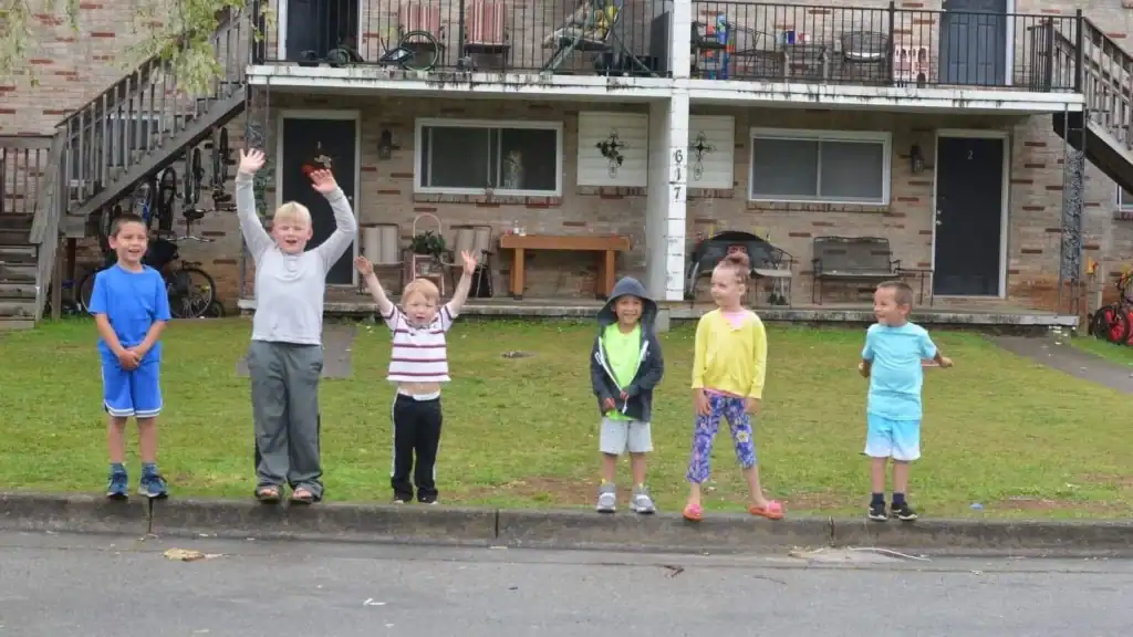 Group of children and an adult playing outside in front of a residential building.