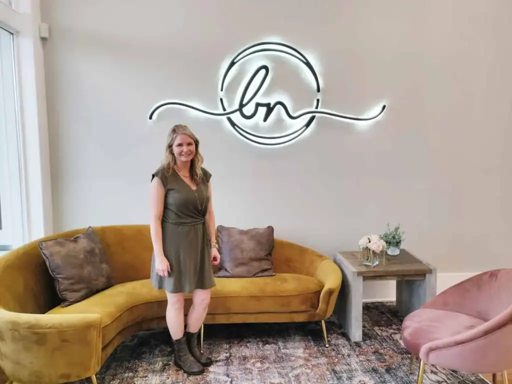Woman standing in modern lounge with neon art and velvet furniture.