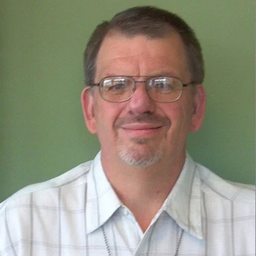 Professional portrait of a man in a white shirt with glasses, smiling.
