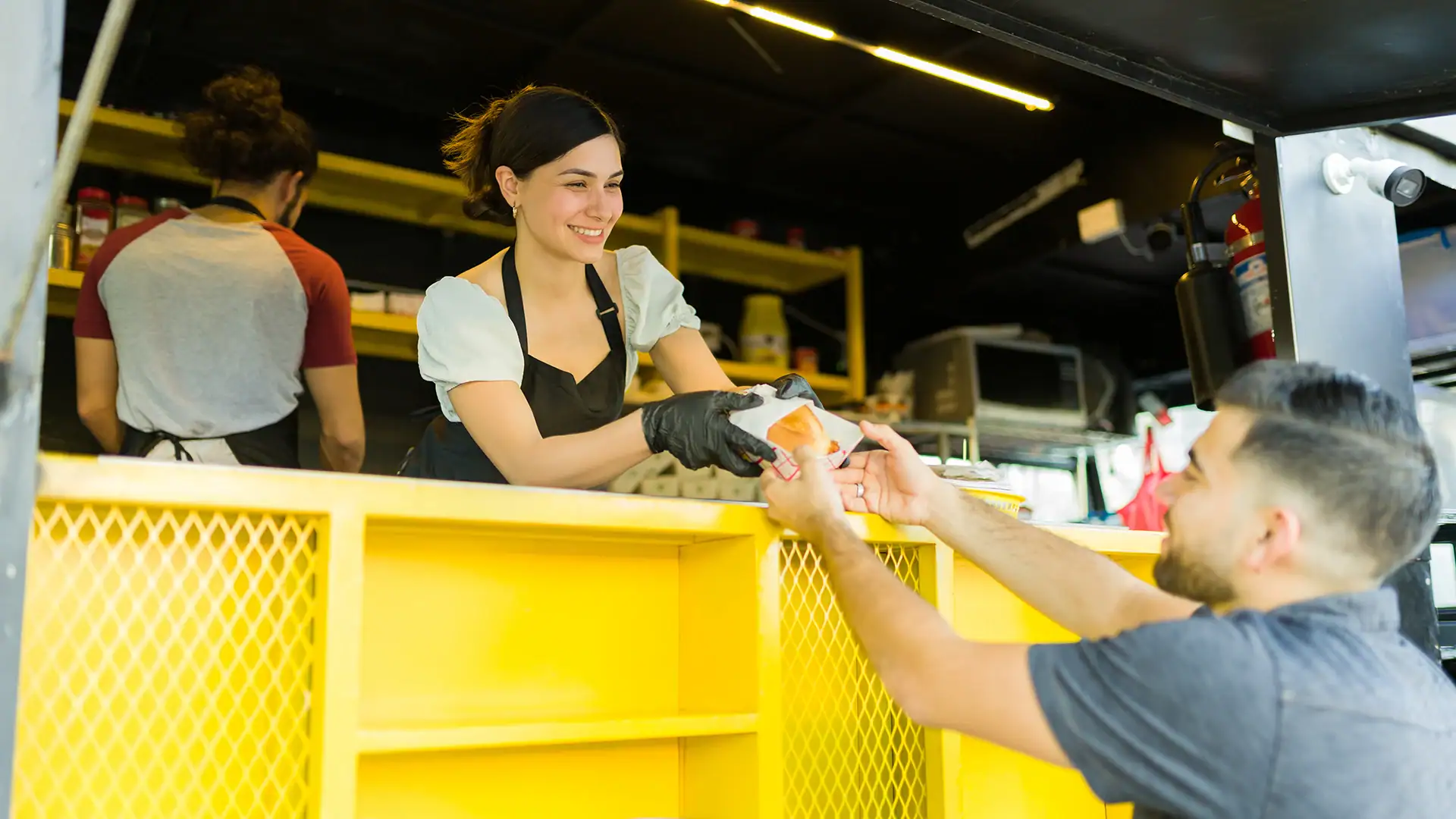 Female vendor handing food to male customer at food truck counter.