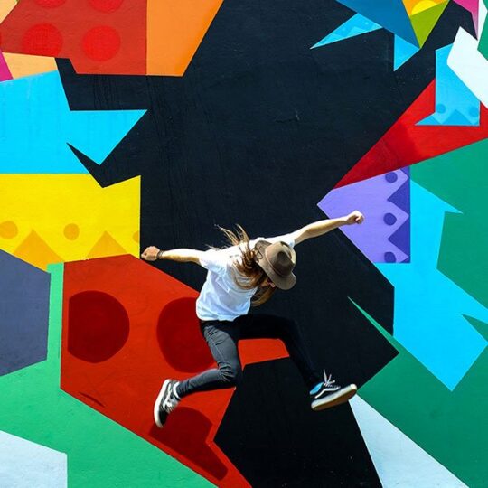 A person jumping in front of a colorful geometric mural wall.