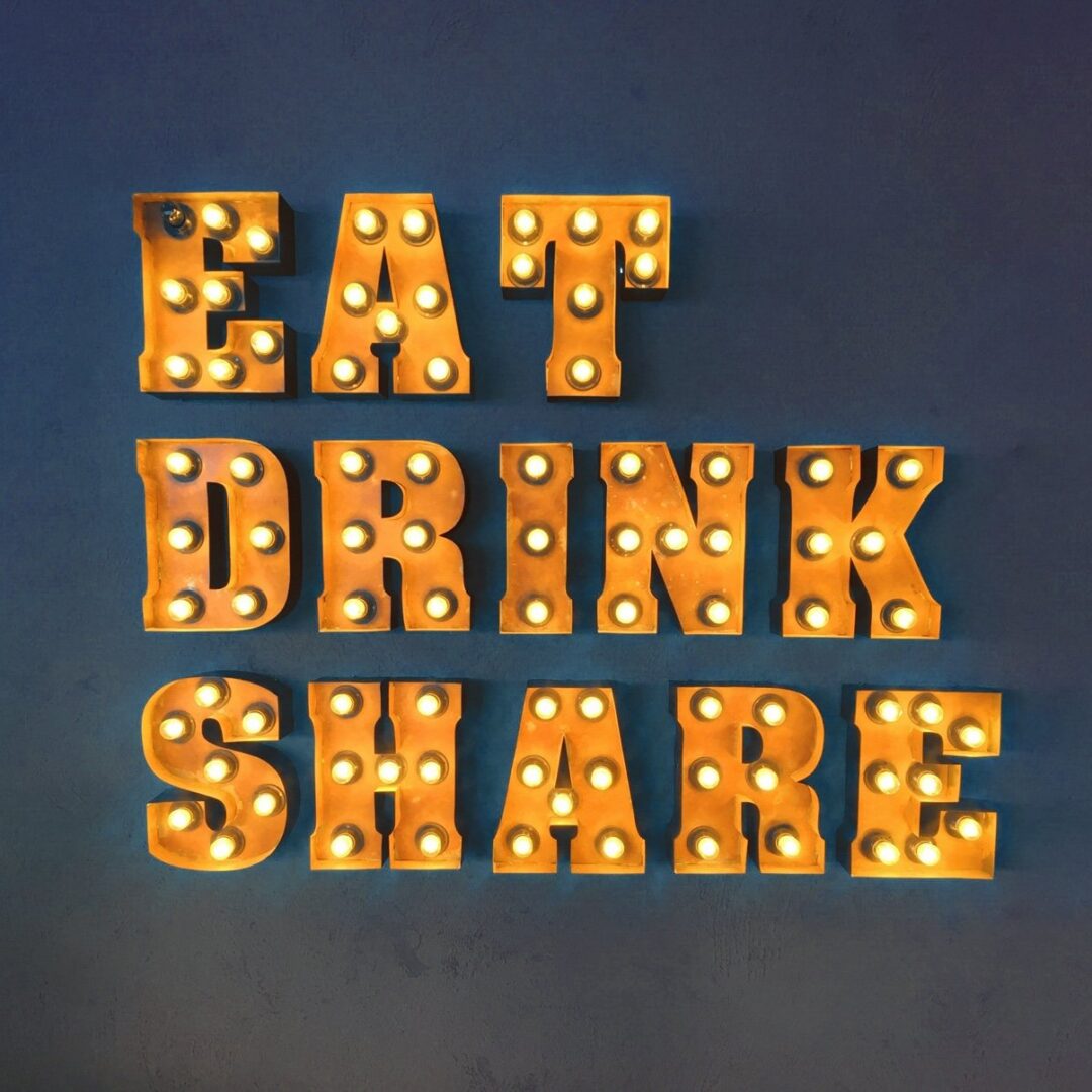 Eat Drink Share illuminated marquee letters on a dark wall.