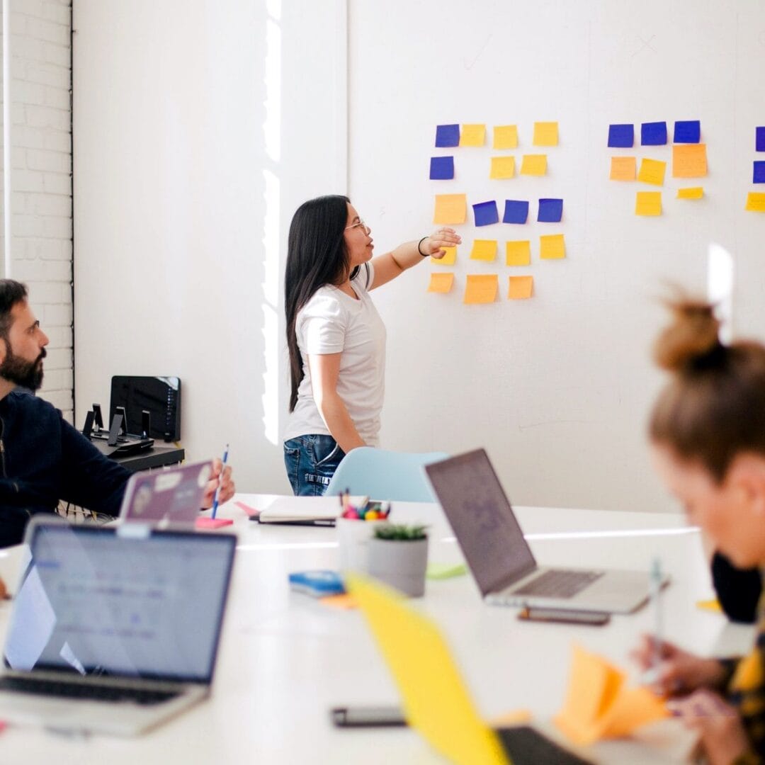 A woman presenting sticky notes on a whiteboard during a team meeting in a modern office.
