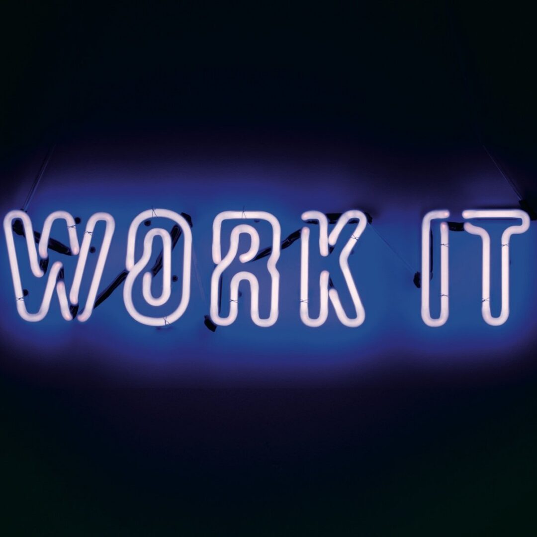 WORK IT neon sign in blue and white light against a dark background.