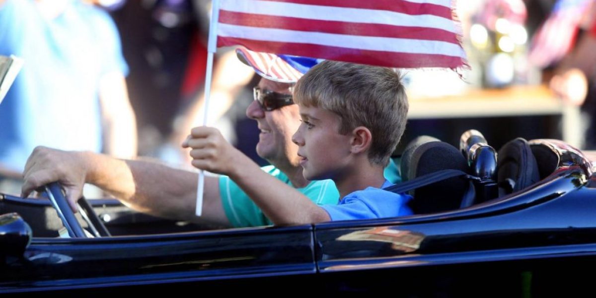 American flag being held by a father and son during a classic car parade in New Zealand.