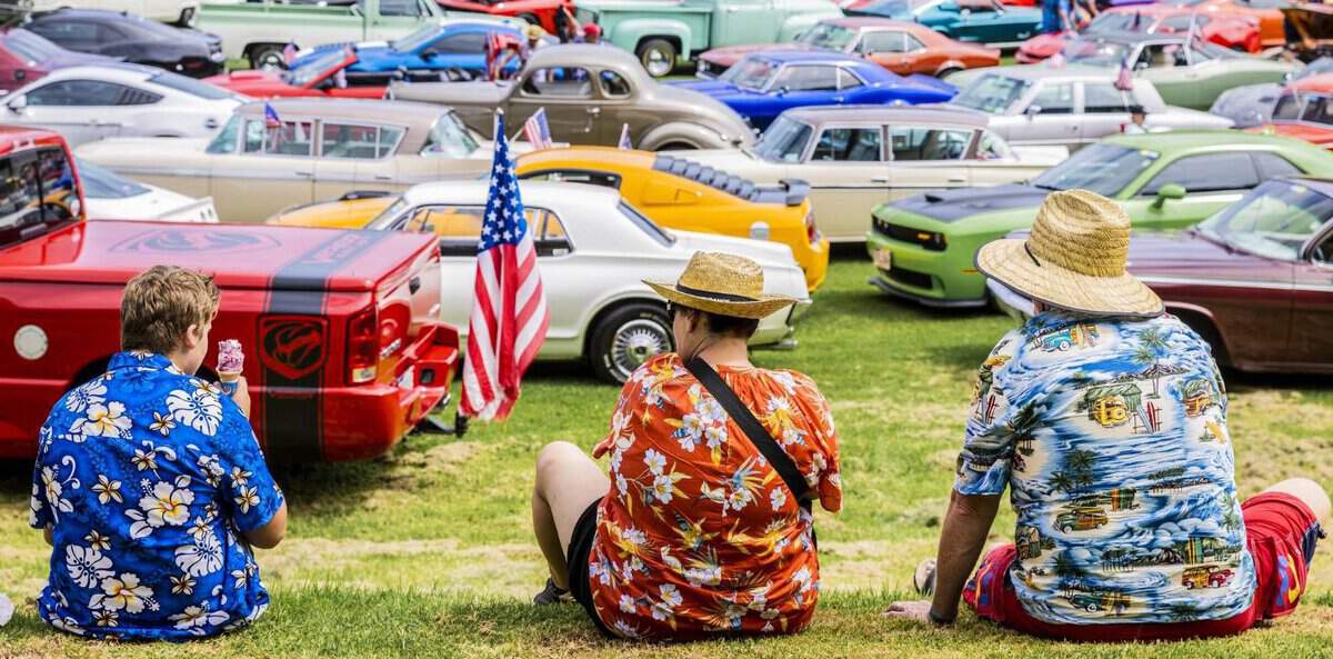 Classic American cars at Americarna event in New Zealand, vintage car show with enthusiasts frolicking, colourful automobiles park on grass.