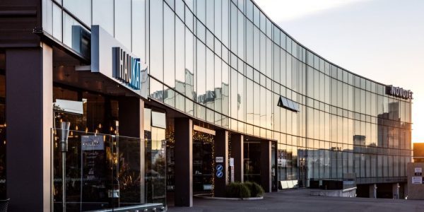Novotel New Plymouth Hobson Modern glass building exterior reflecting city skyline at sunset.