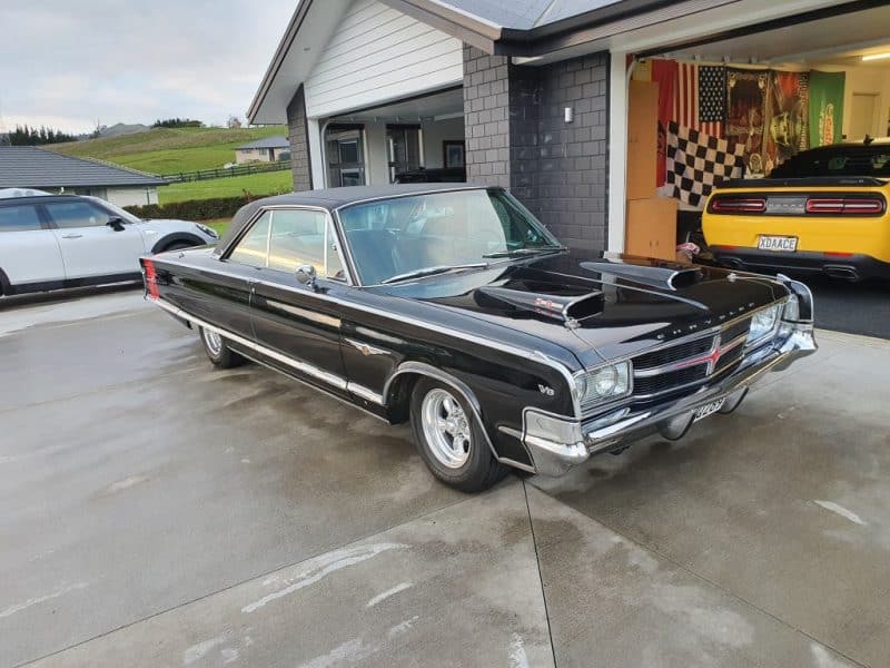 Black classic muscle car with hood scoops in driveway, American car enthusiast home, vintage automobile collection.