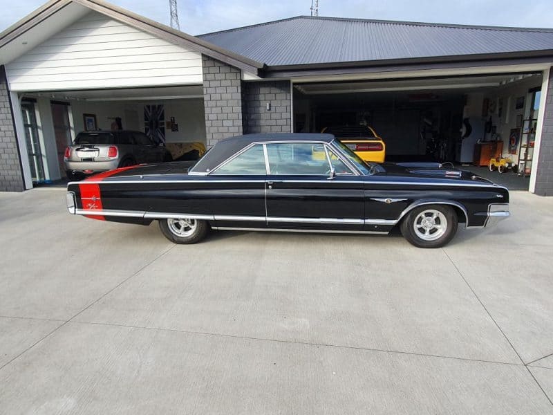 Classic black 1960s muscle car with red racing stripe parked outside garage, vintage American car restoration.
