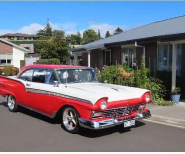 Classic red and white vintage car parked in suburban street, showcasing American car culture.