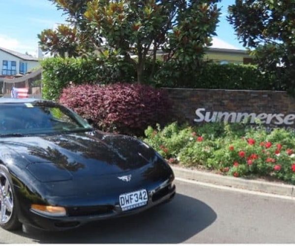Black Chevrolet Corvette sports car parked in front of Sunerset sign at Americarna event in New Zealand.
