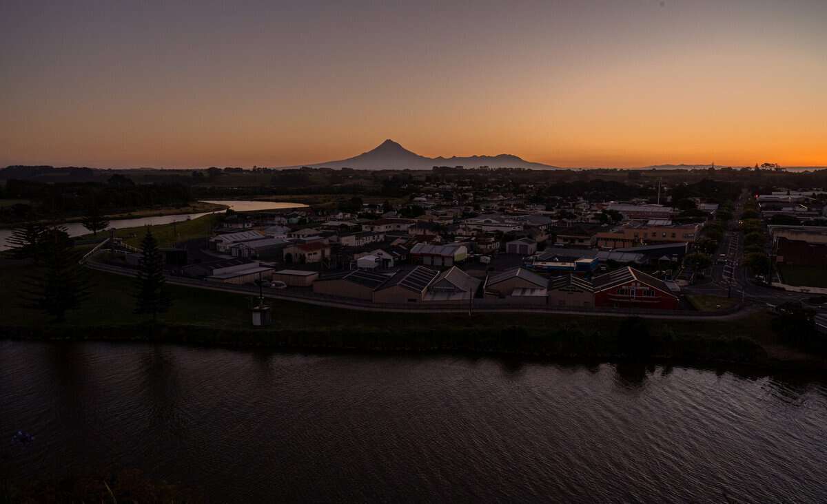 Sunset over a coastal town with Mount Taranaki in the background, capturing scenic New Zealand landscape and community.
