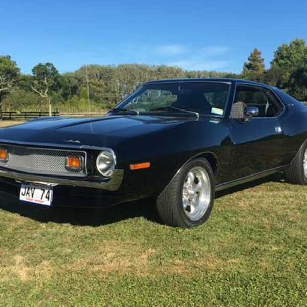 Classic black vintage muscle car parked on grass under clear blue sky at Americarna event.