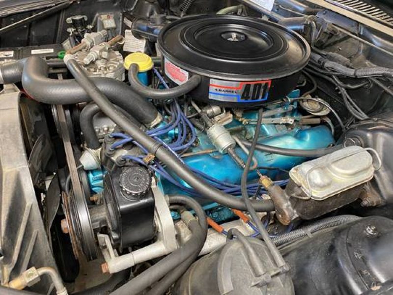 V8 engine with blue components and air filter in classic American muscle car.