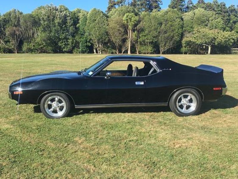 Black vintage muscle car parked on grass under trees.