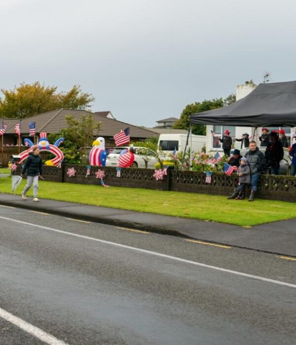 Decorated American caravan parade with flags, inflatable figures, and spectators celebrating patriotic event.
