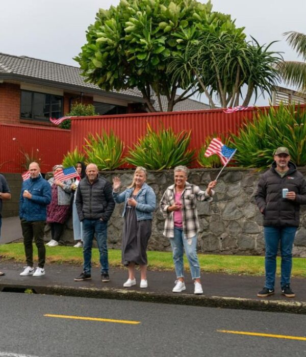 Colourful American-themed street parade with people holding American flags in New Zealand, celebrating US culture and community.