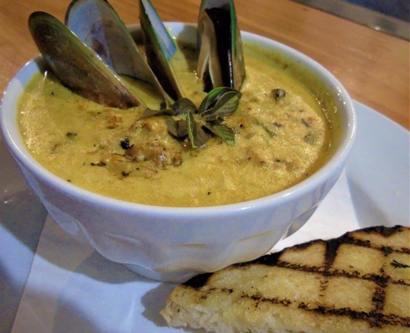 Creamy New Zealand mussel chowder in a white bowl, served with grilled flatbread. Classic American seafood dish with fresh ingredients.