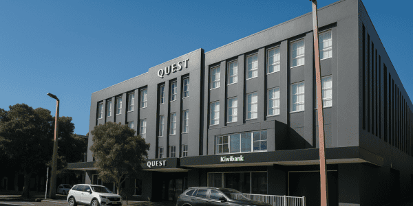 ChatGPT Image May 17, 2025, 10_17_32 AM Modern grey Quest building with Kiwibank signage and parked cars in front, clear blue sky, New Zealand commercial architecture.