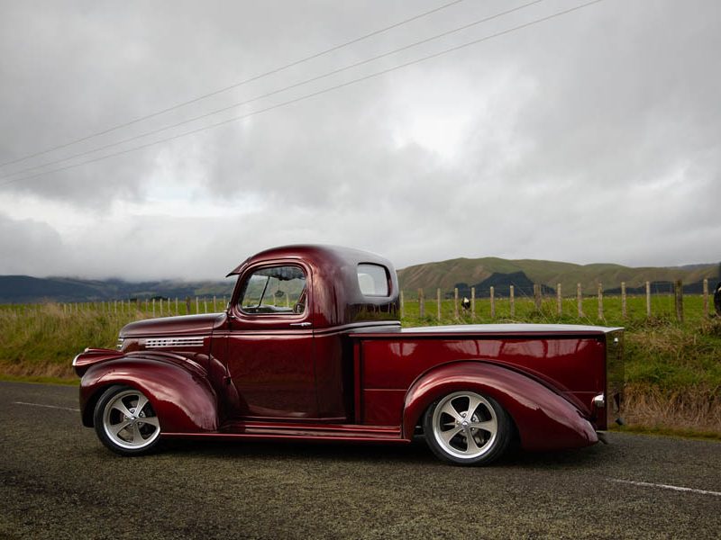 Classic American vintage truck in New Zealand countryside with custom wheels and red paint.