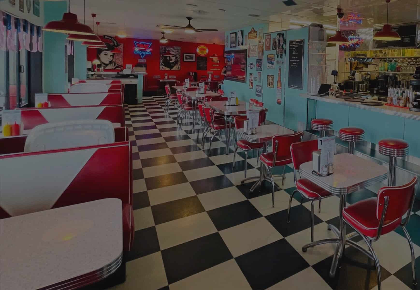 Interior of classic American diner with red chairs, checkered floor, and vintage wall art.