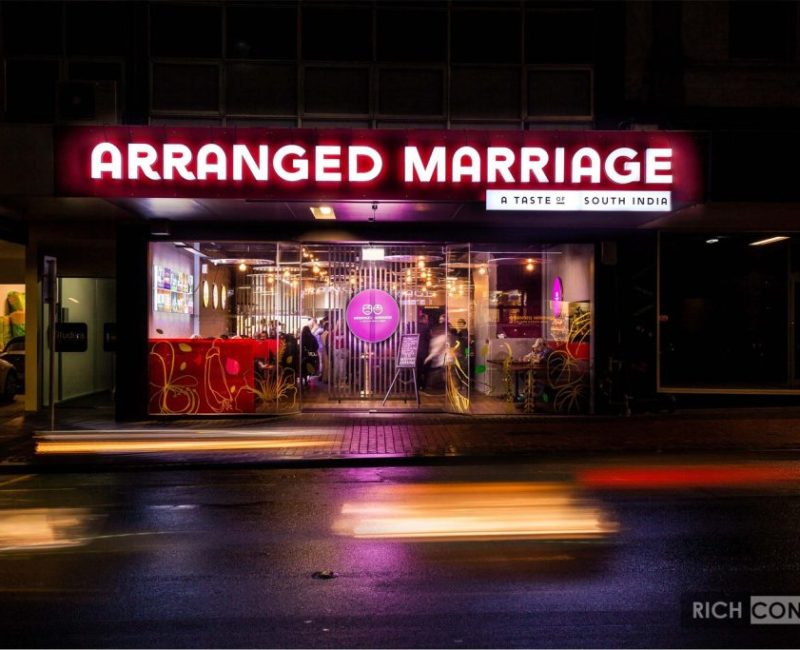 Neon sign outside Arranged Marriage Indian restaurant at night, lively atmosphere.