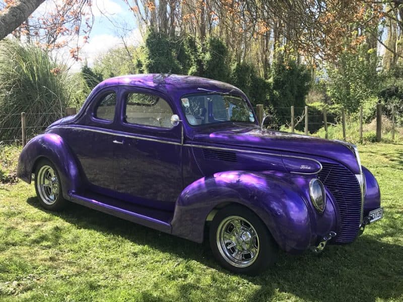 Unique purple classic Ford vehicle on lush green grass.
