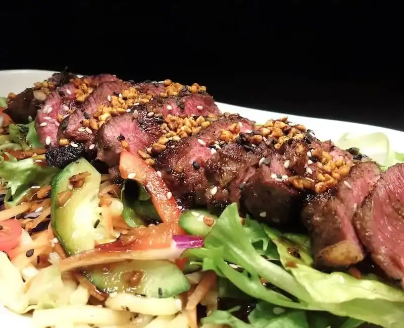 Delectable grilled beef slices on fresh mixed salad with crunchy vegetables and sesame seeds, perfect for a flavourful healthy meal.