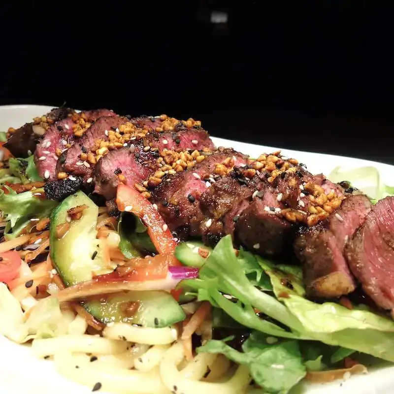 Delectable grilled beef slices on fresh mixed salad with crunchy vegetables and sesame seeds, perfect for a flavourful healthy meal.