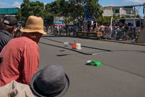 Vibrant green race car speeds past spectators during Americarna event in New Zealand.