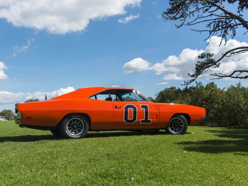 Vintage American muscle car in bright orange with racing decals, showcased at Americarna event.