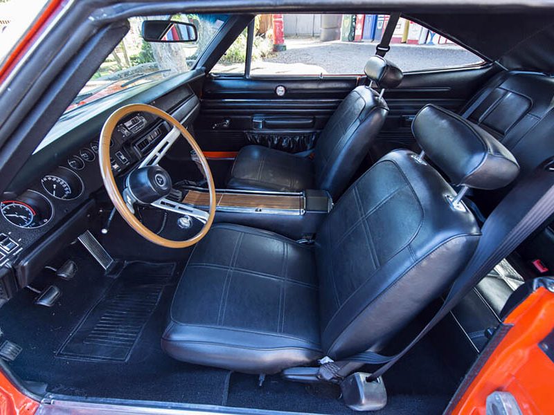 Interior view of a vintage American car showcasing black leather seats, wooden steering wheel, and dashboard gauges.