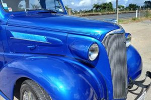 Blue vintage car parked outdoors with scenic sky background in New Zealand.