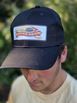 A young man wearing a navy blue Americarna cap featuring the event logo outdoors.