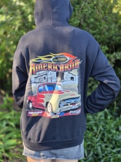 Casual person wearing a navy hoodie with a colorful Americarna car graphic, outdoors in a green setting.