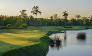 Lush golf course beside tranquil water.