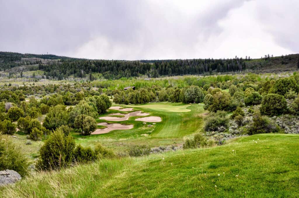Scenic view of a golf course surrounded by lush greenery and rolling hills.