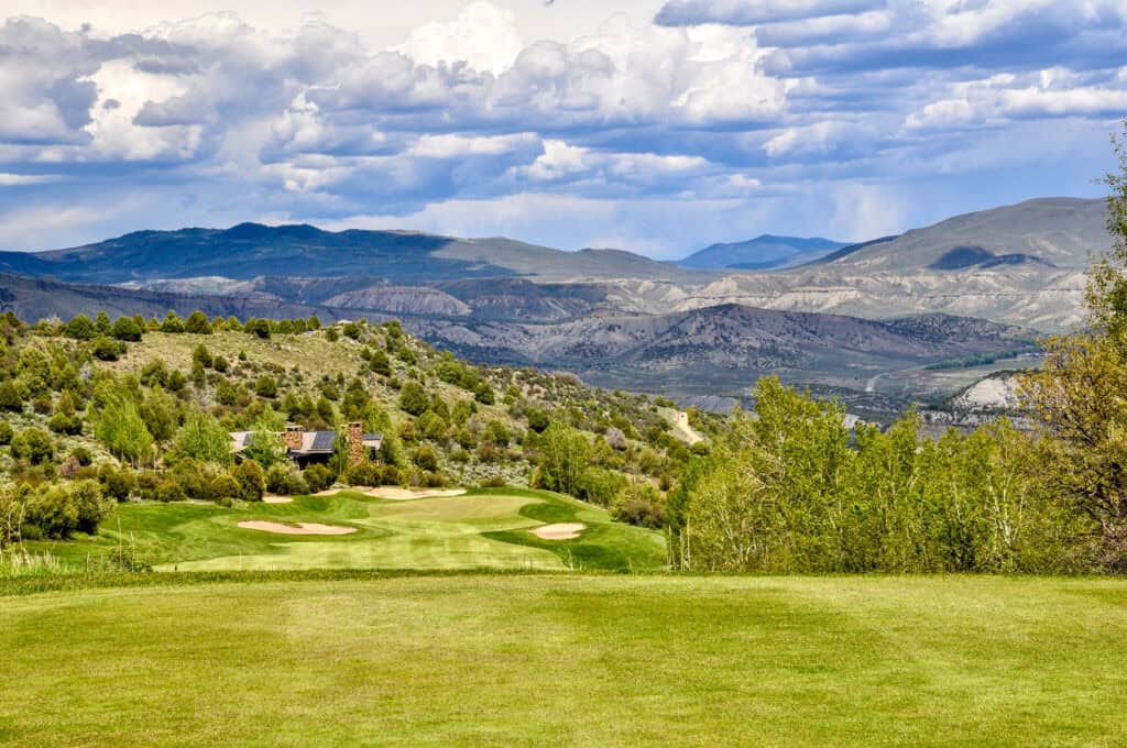 Scenic mountain landscape with a lush green golf course in foreground.